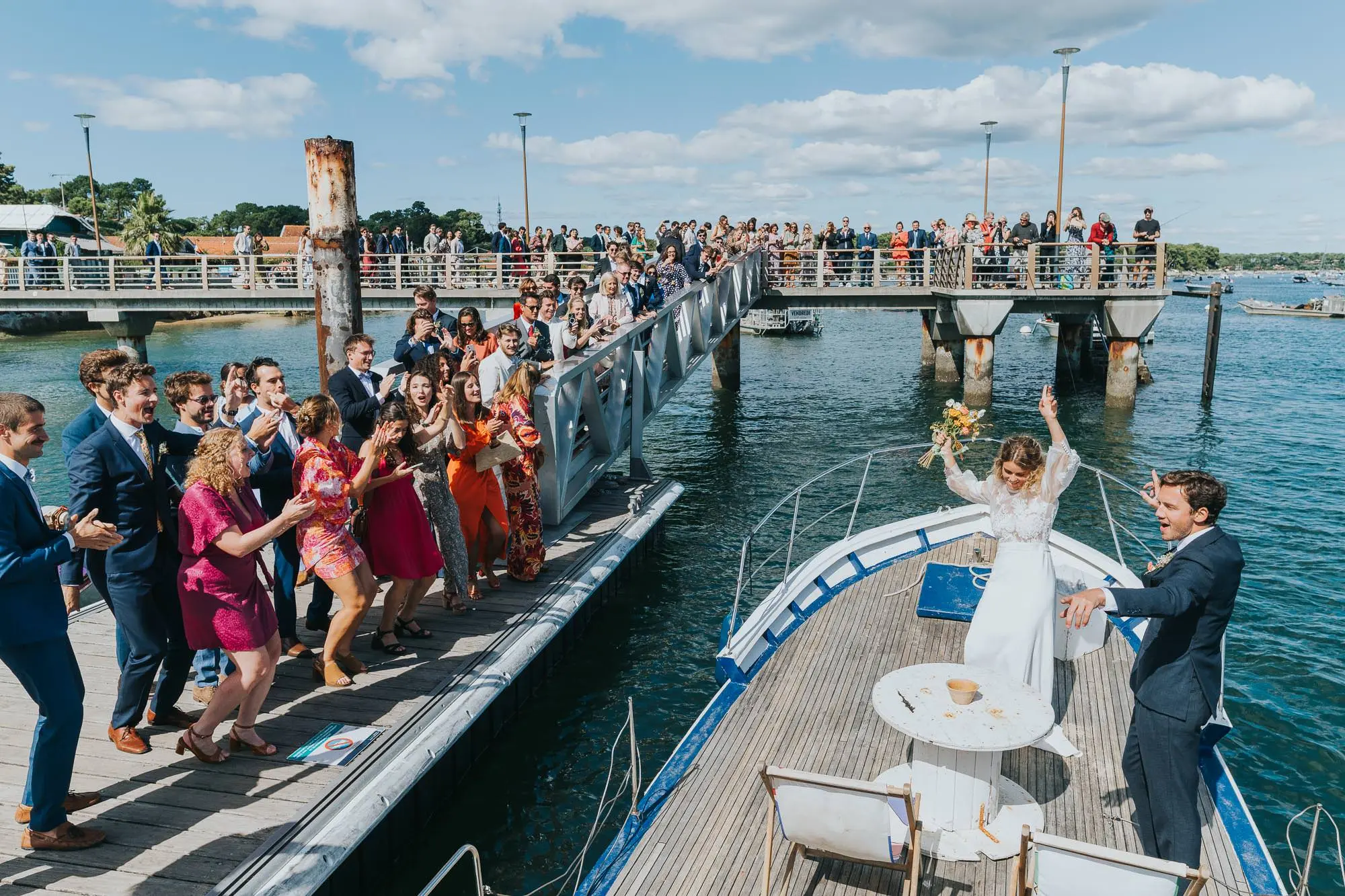 Couple de mariés partant en bateau sous les applaudissements des invités sur le Bassin d’Arcachon photographe mariage Bordeaux