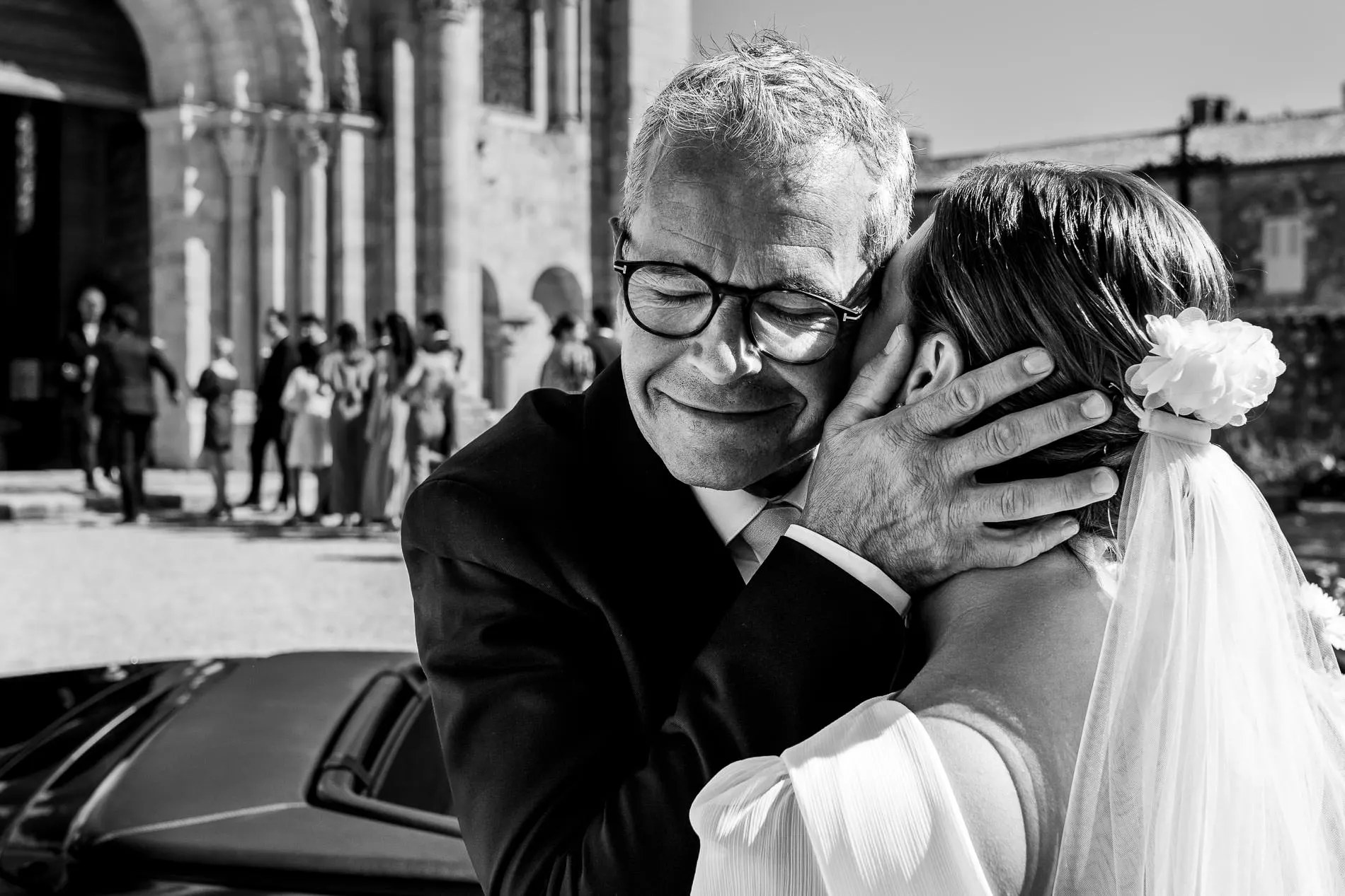 Père ému serrant sa fille mariée dans ses bras à la sortie de l’église photo mariage Gironde
